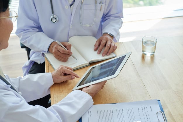 Doctor taking notes as he inspects an iPad in the hands of female doctor.